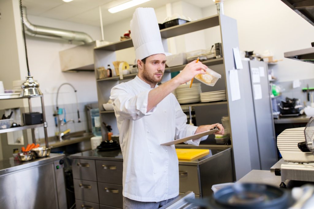 cooking, profession and people concept - male chef cook with clipboard doing inventory in restaurant kitchen