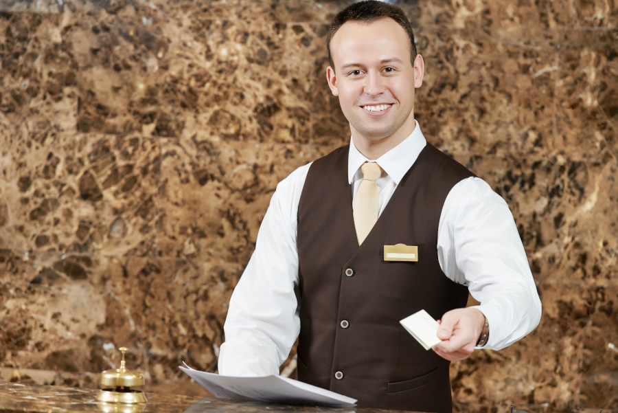 smiling male receptionist passing key card to guest