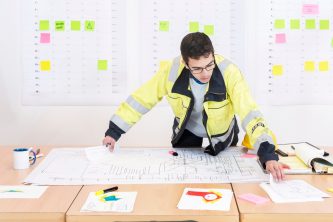 Construction worker checking design drawings in an office, wearing a saftety jacket
